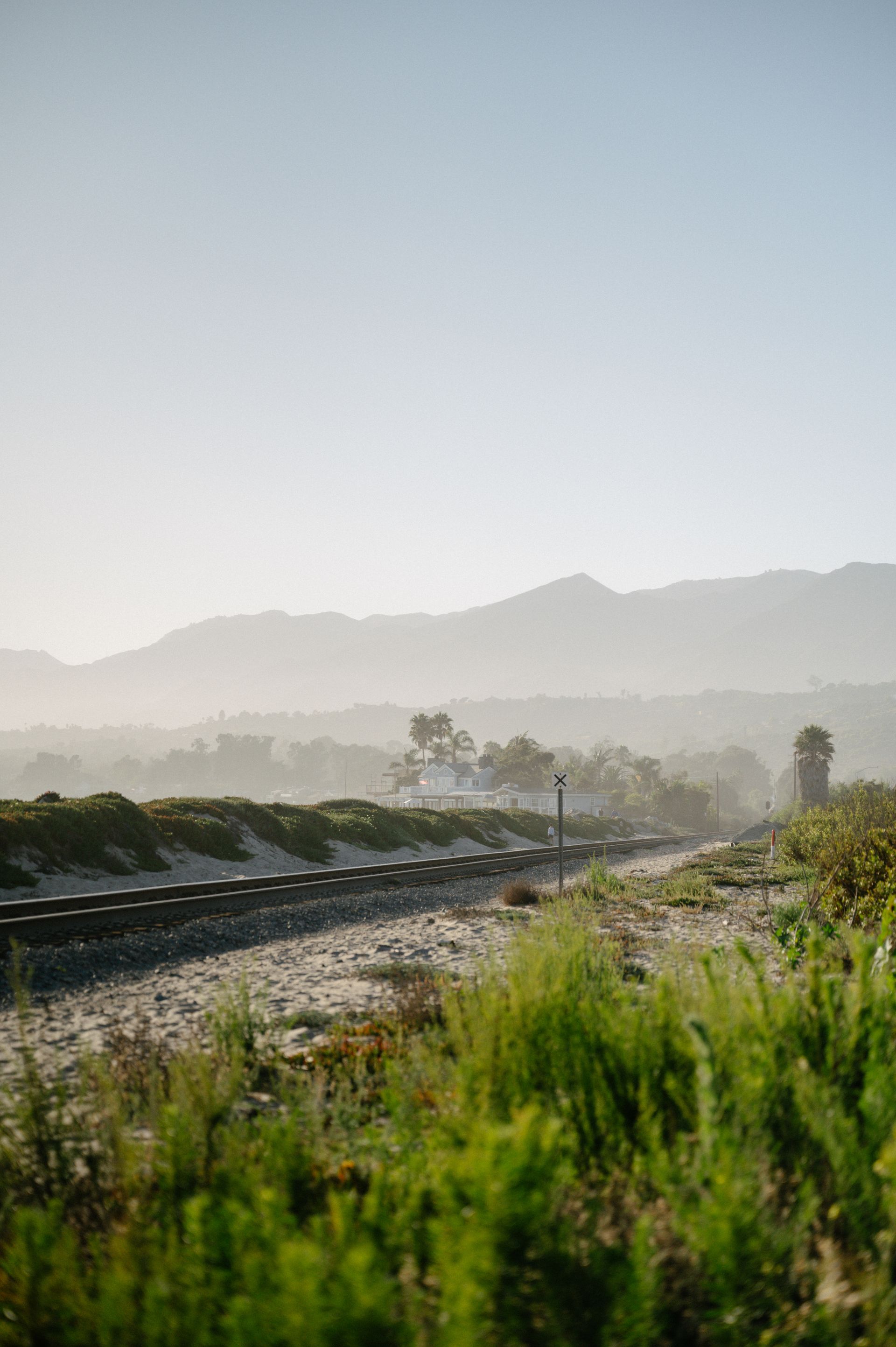 Sunlit railway tracks curving through green fields with hazy mountains in the distance