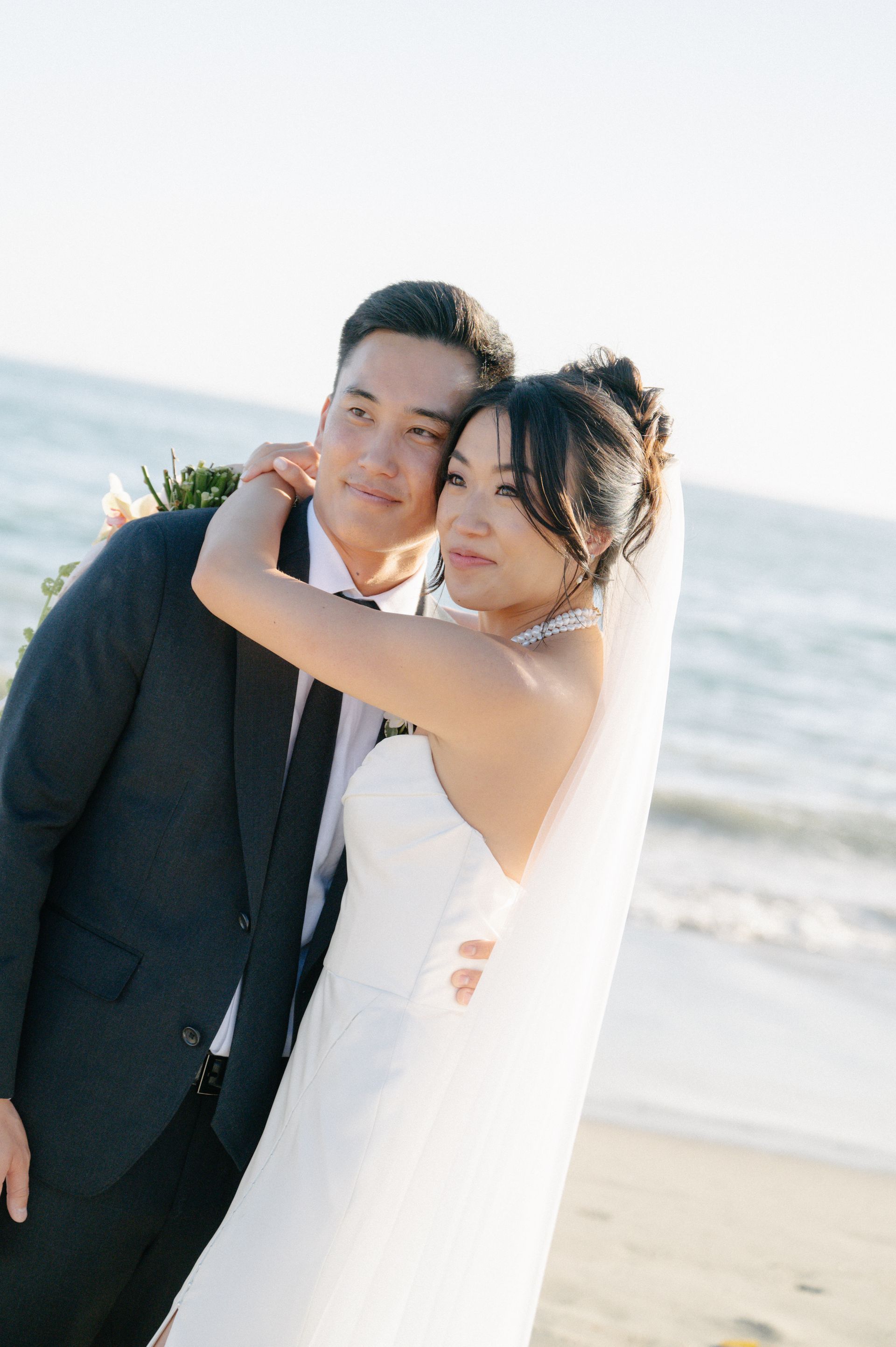 Couple in wedding attire embracing on a beach at sunset