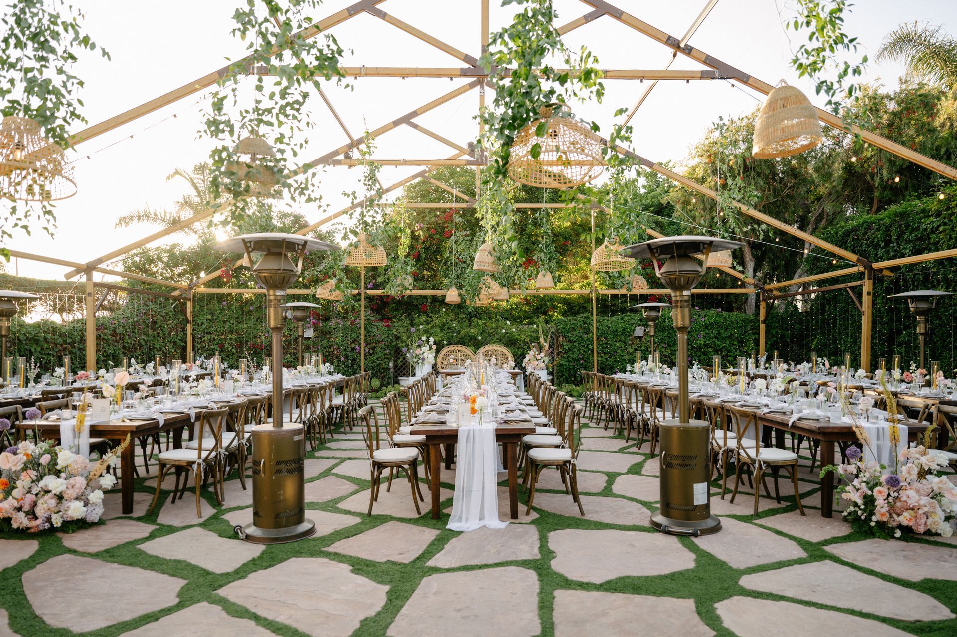 Elegant outdoor wedding reception under a tent with long banquet tables, greenery, and string lights