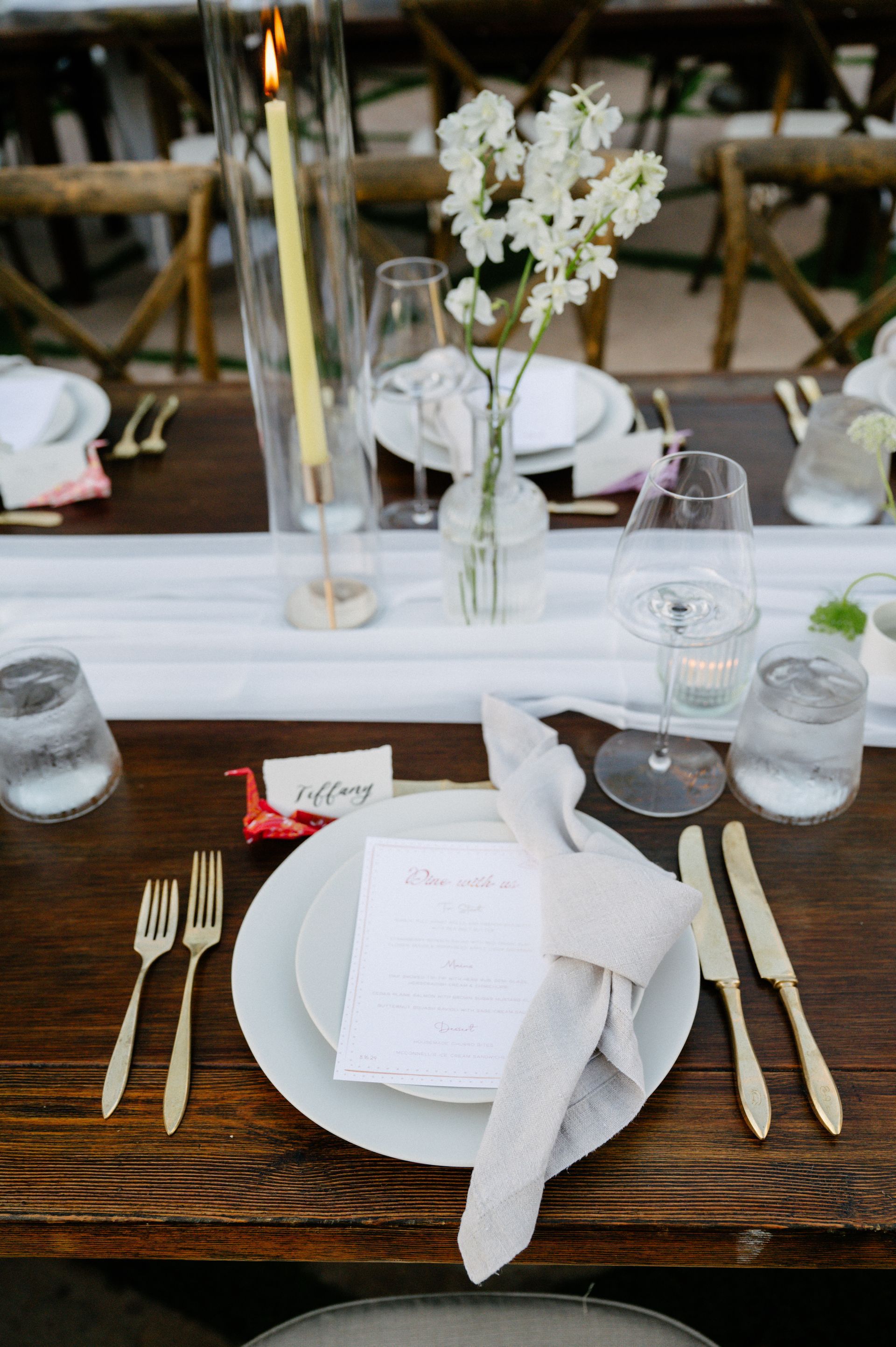 Elegant white table setting with candles, glassware, folded napkins, and a small floral centerpiece