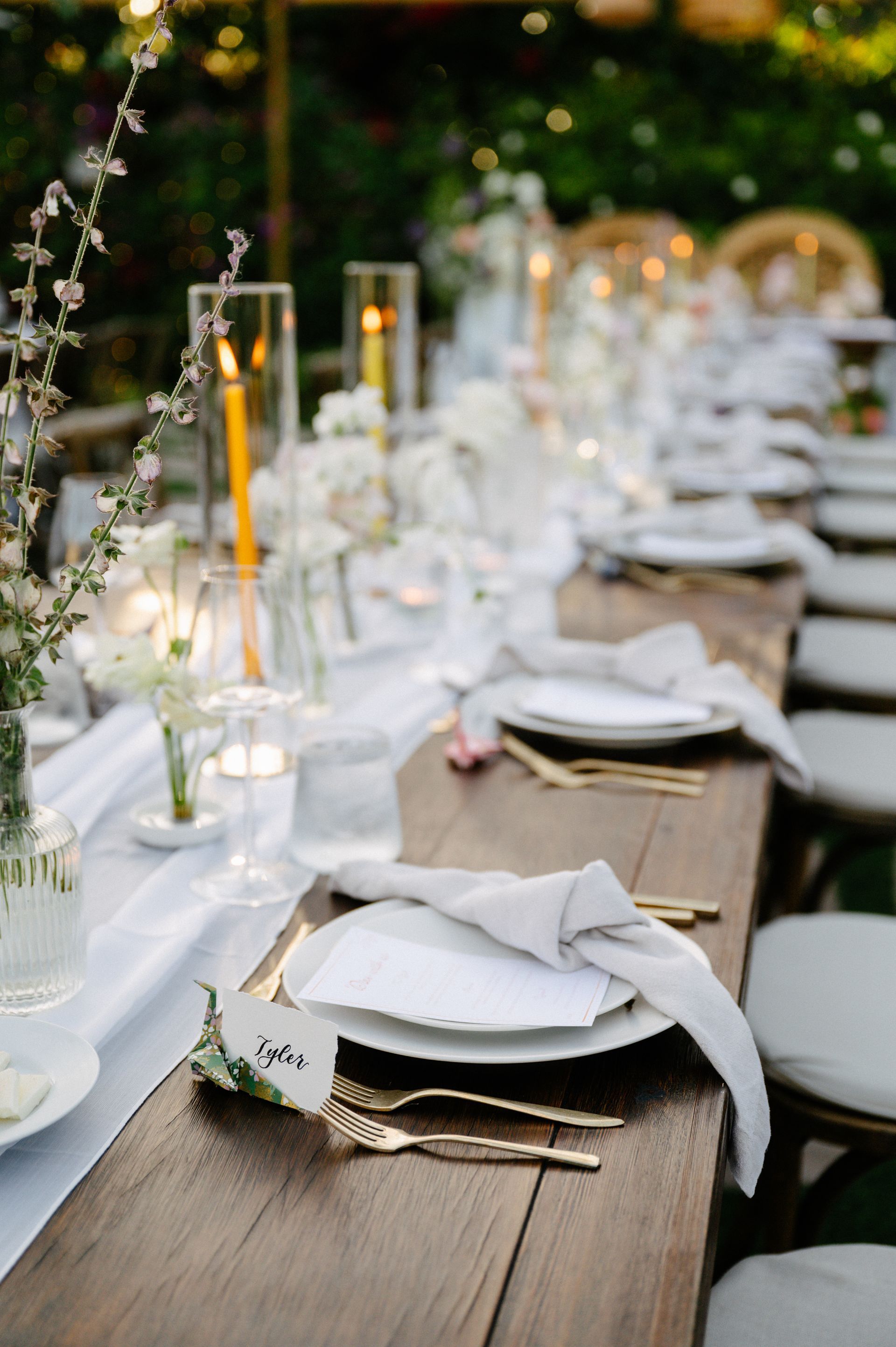 Elegant outdoor dining table with white napkins, candles, and glassware set for a wedding reception