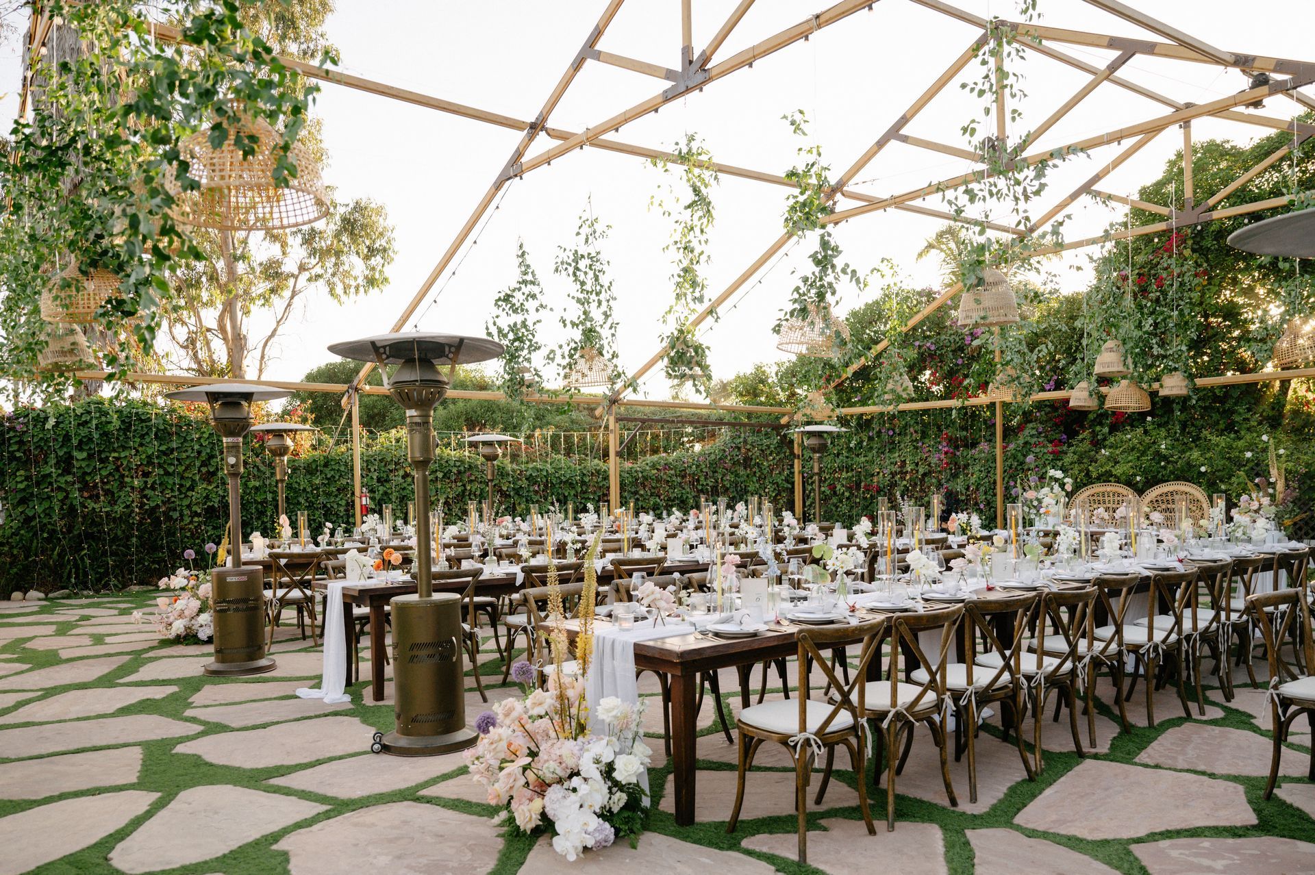 Elegant outdoor dining setup under a canopy with long tables, white linens, flowers, and stone-paved flooring