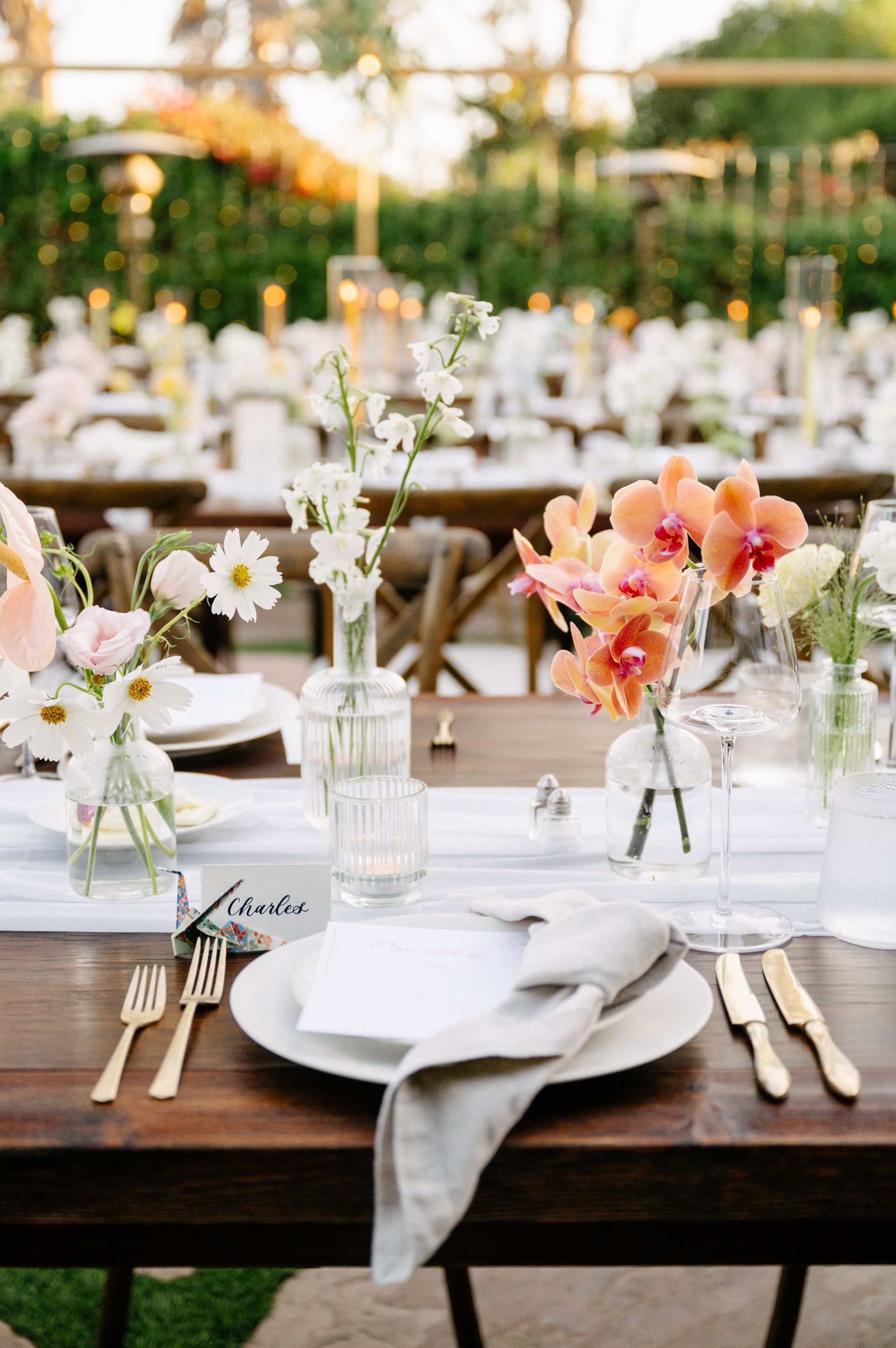 Elegant outdoor wedding reception table with white flowers, gold flatware, and peach floral arrangements