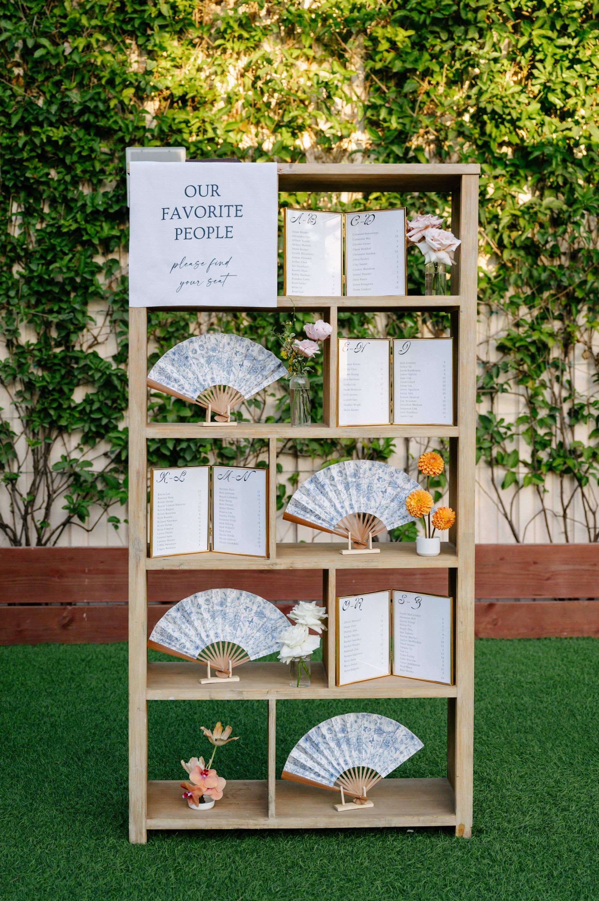 Decorative display shelf with paper fans and cards against a green ivy wall