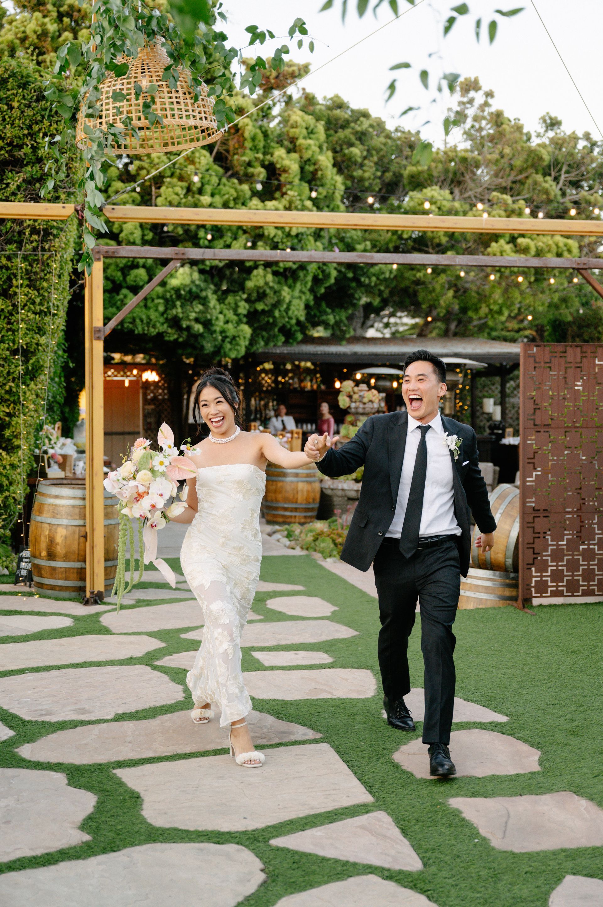 Bride and groom holding hands and dancing down a stone path in an outdoor garden venue