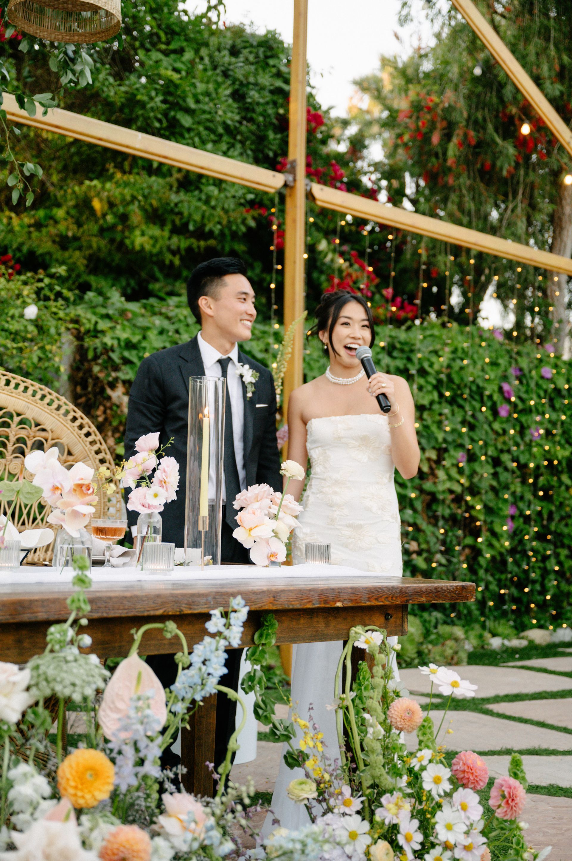 Wedding couple toasting at a decorated outdoor reception table with flowers and greenery