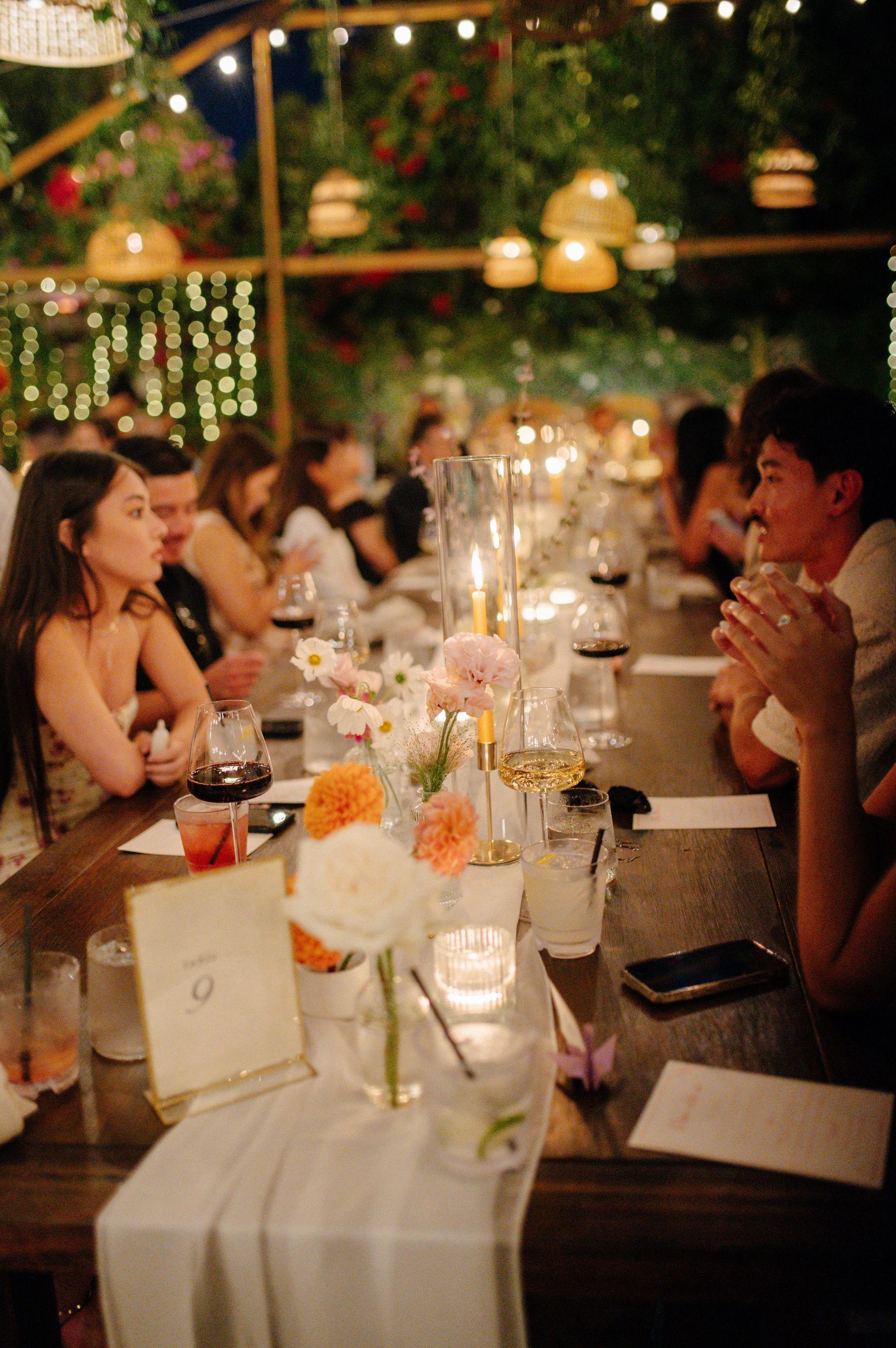 People dining at a warmly lit candlelit dinner table with flowers and drinks