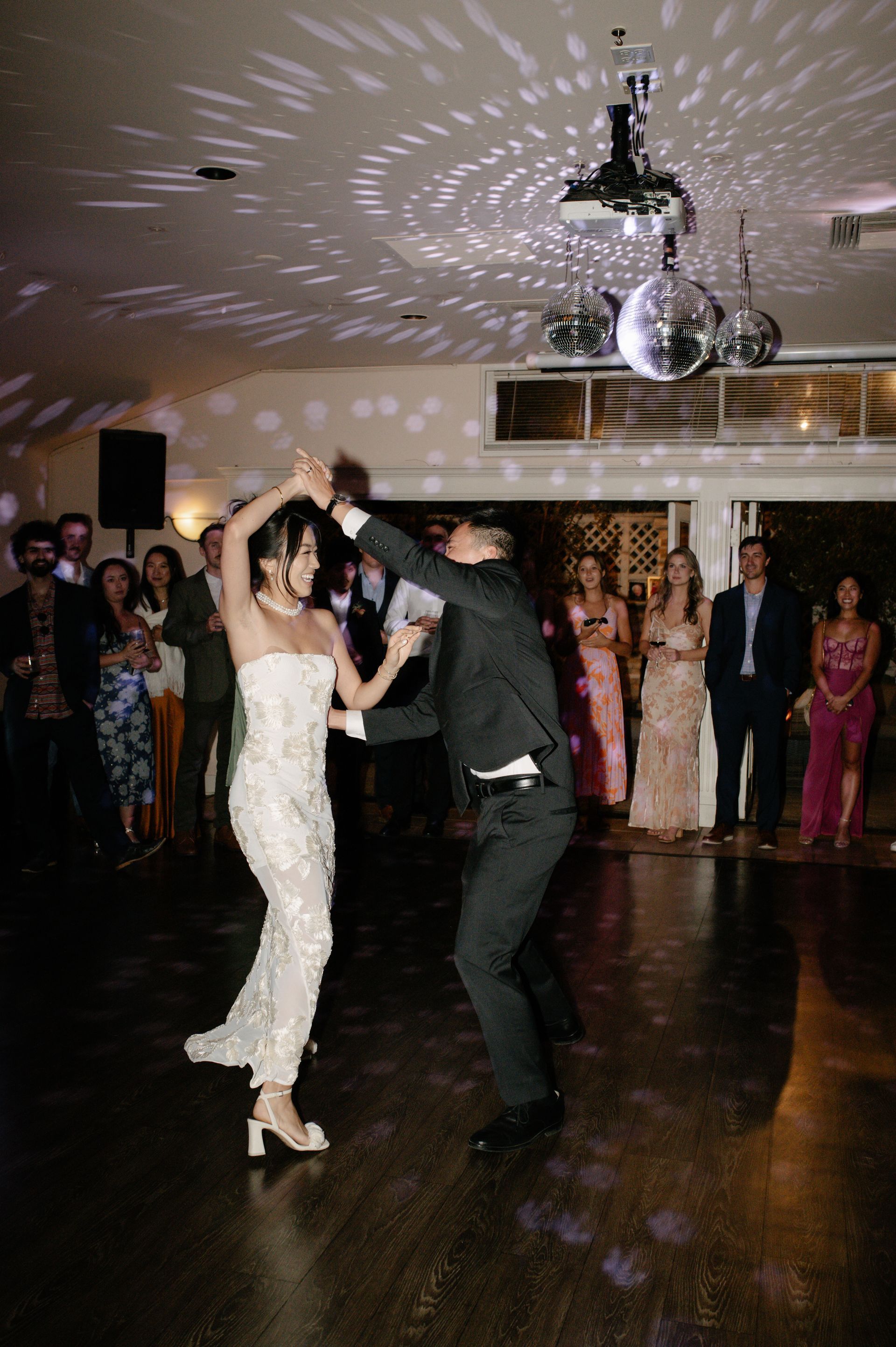 Couple dancing at a formal indoor event with guests watching in the background
