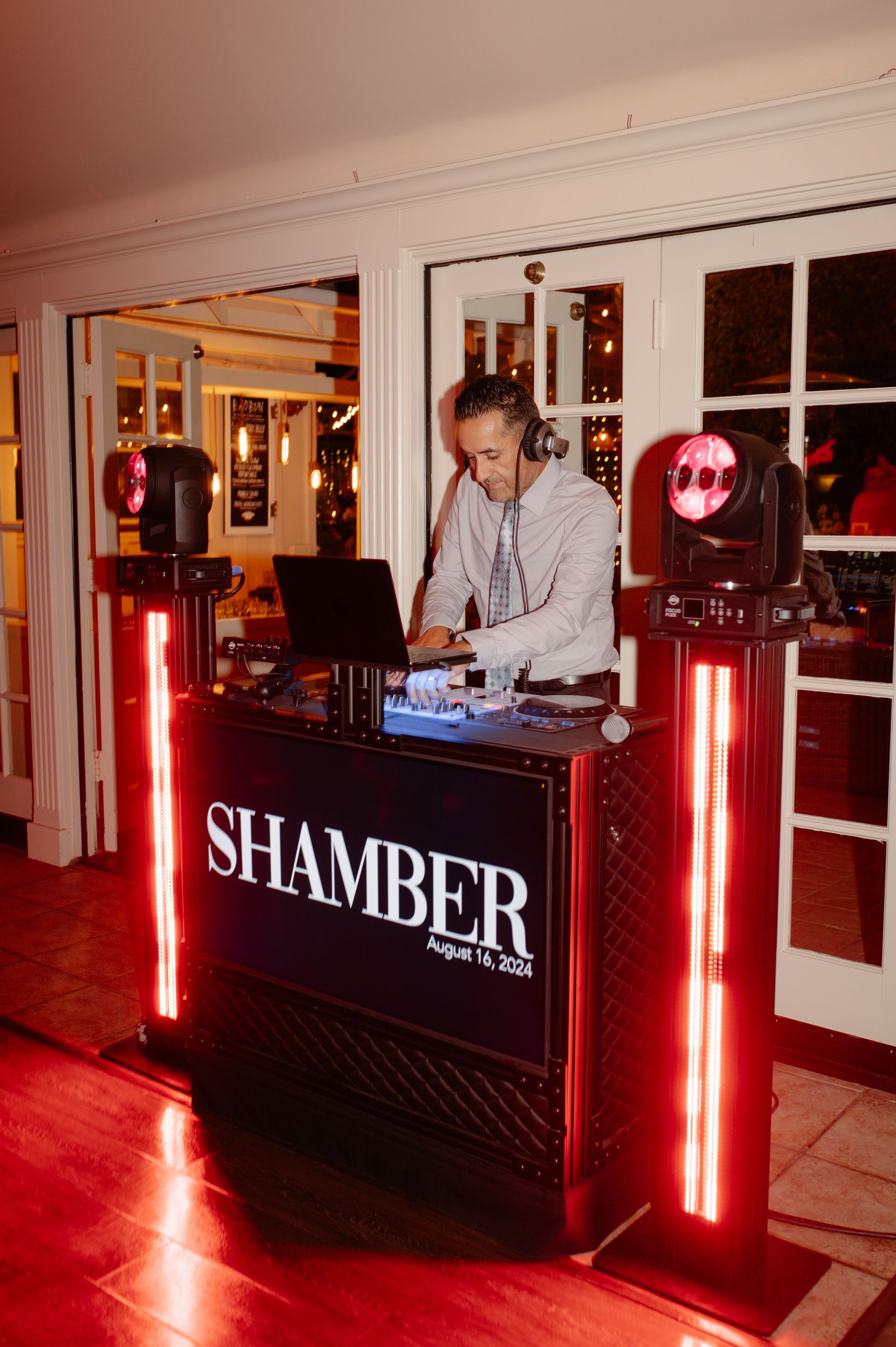 DJ behind a black SHAMBER booth with red lights in a warmly lit room
