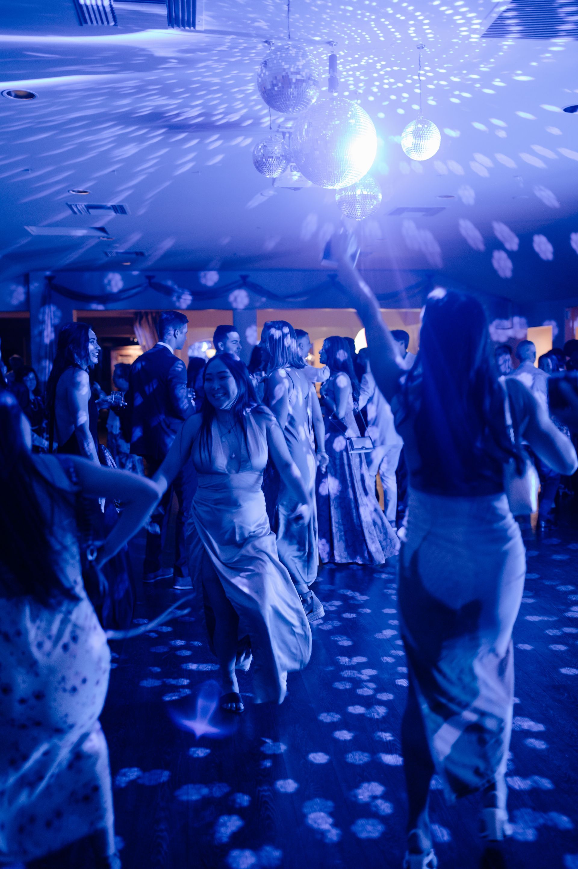 Blue-lit dance floor with people dancing under disco lights and a mirrored ceiling