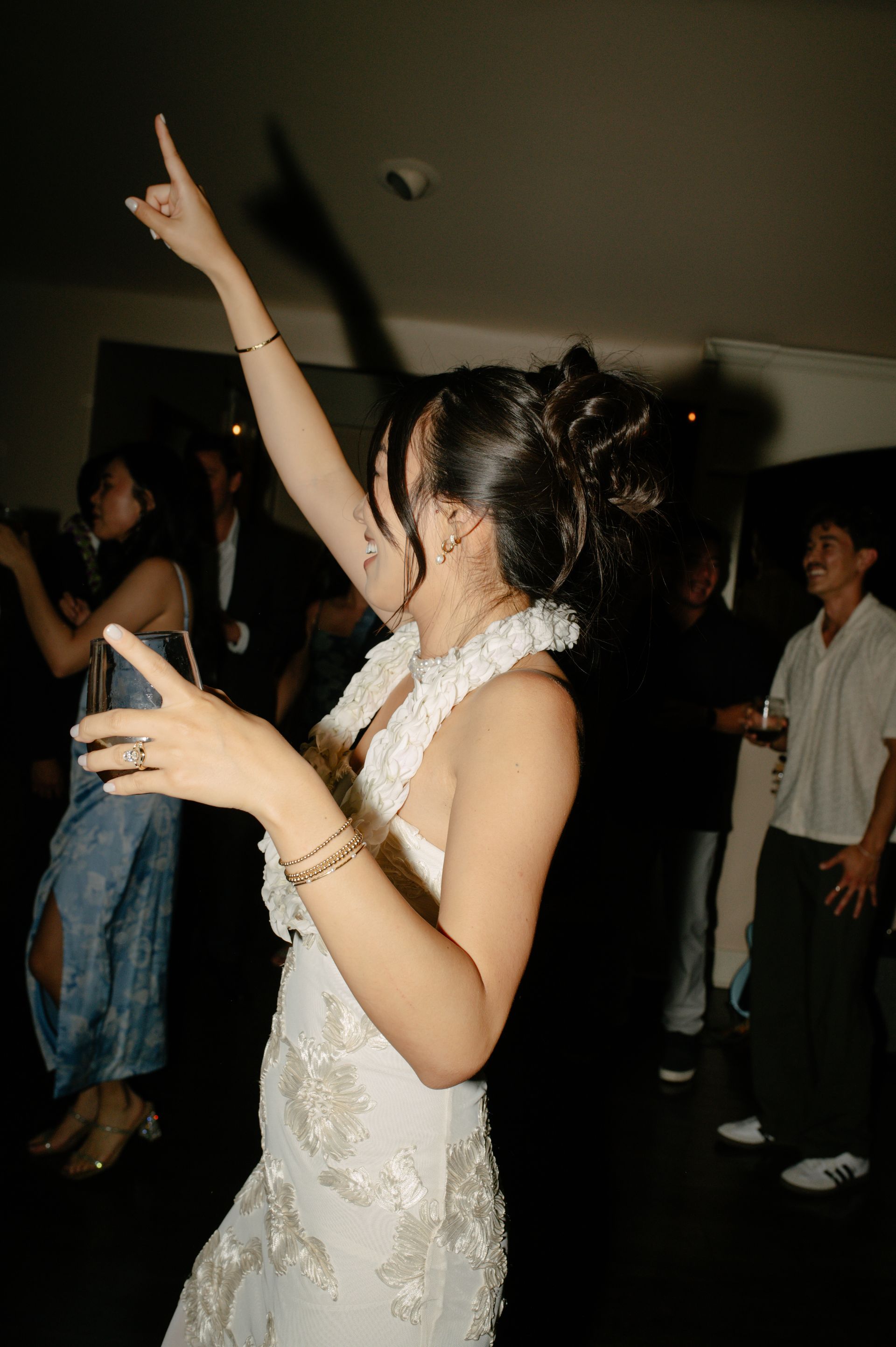 Woman in a white dress dancing at a dimly lit party, one arm raised and smiling.
