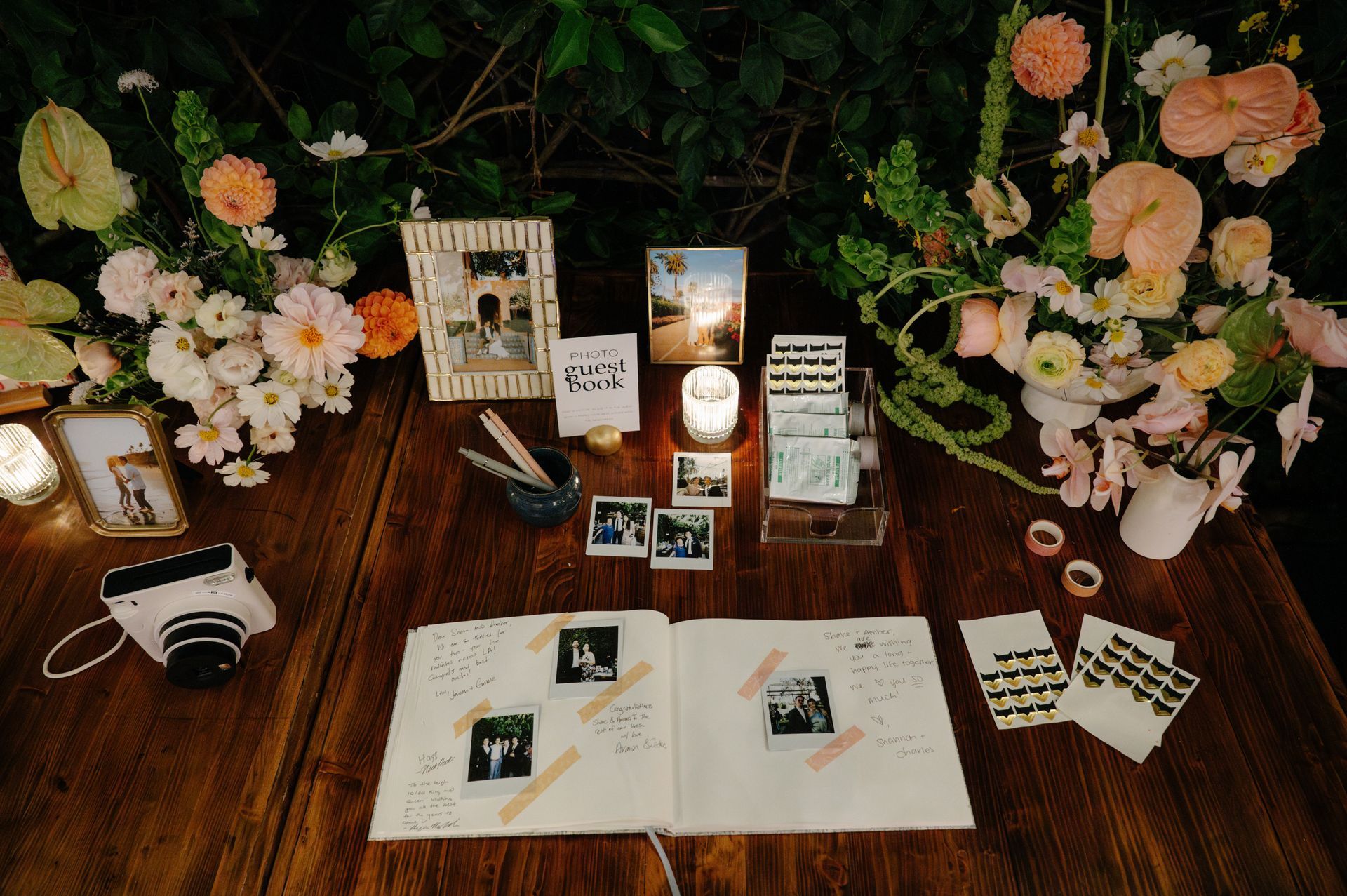 Decorated wooden table with floral arrangements, cards, photos, and a camera in a cozy display