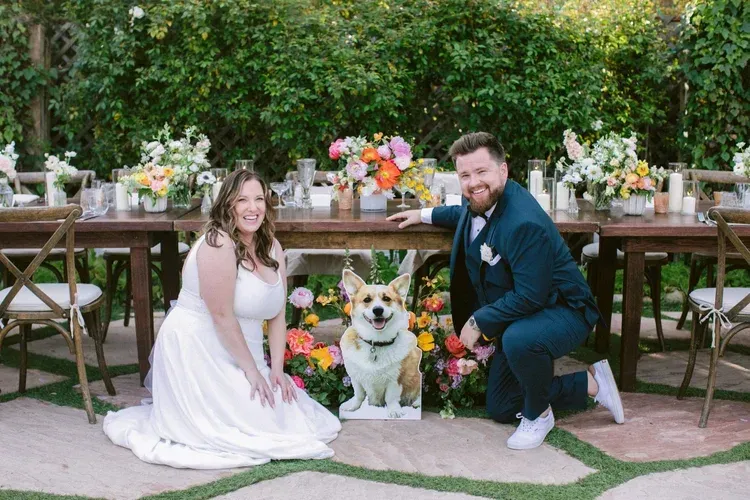 Wedding couple with dog in white floral collar posed outdoors by a decorated table