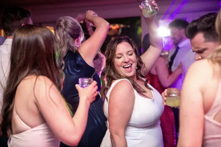 People dancing at a lively nightclub, smiling under purple lights with drinks in hand