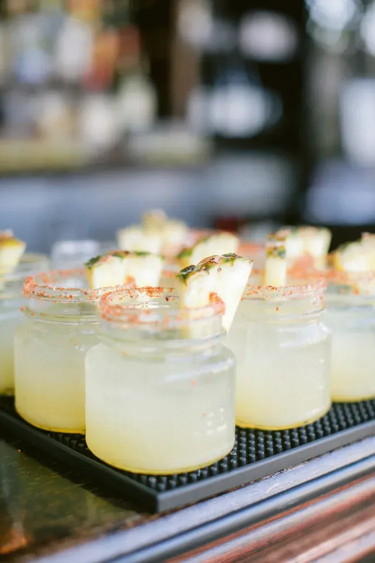 Row of lemon cocktails garnished with herbs on a tray at a bar