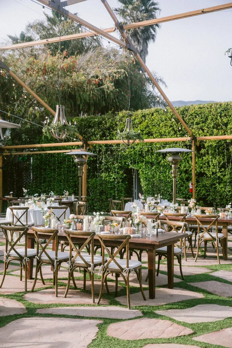 Outdoor dining setup with wooden tables and chairs under a bamboo canopy, surrounded by greenery
