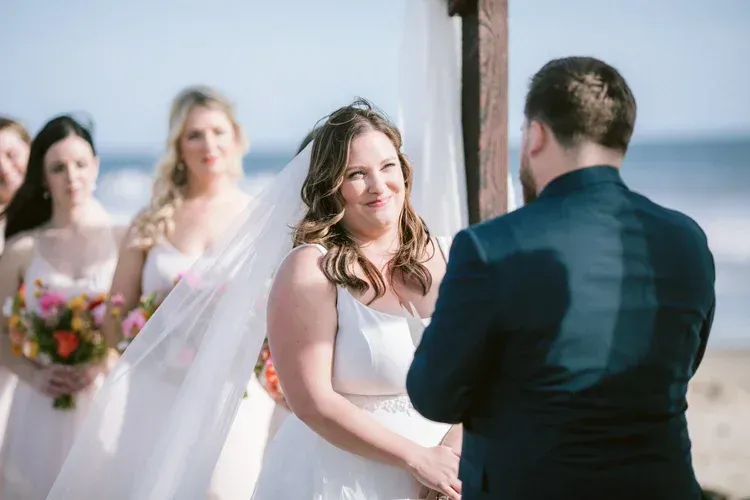 Bride smiling at groom during outdoor wedding ceremony, with bridesmaids holding bouquets in the background