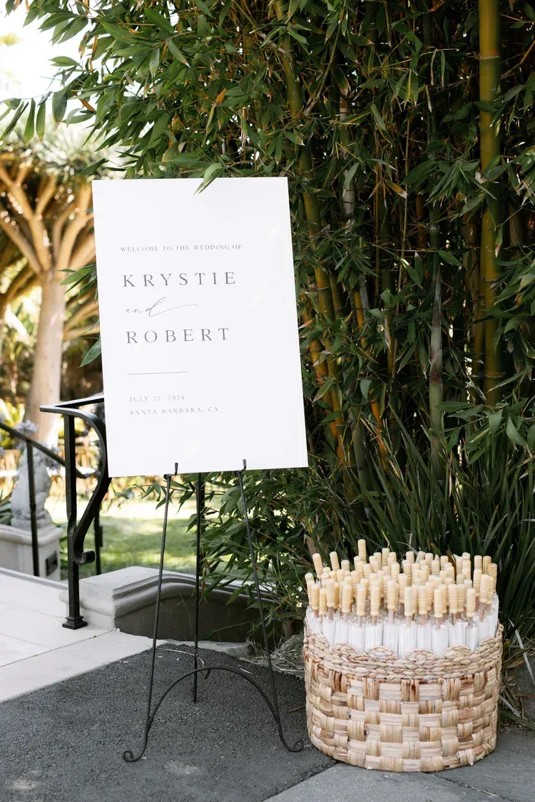 White sign beside a woven basket of cream-colored candles in a bamboo-lined outdoor setting