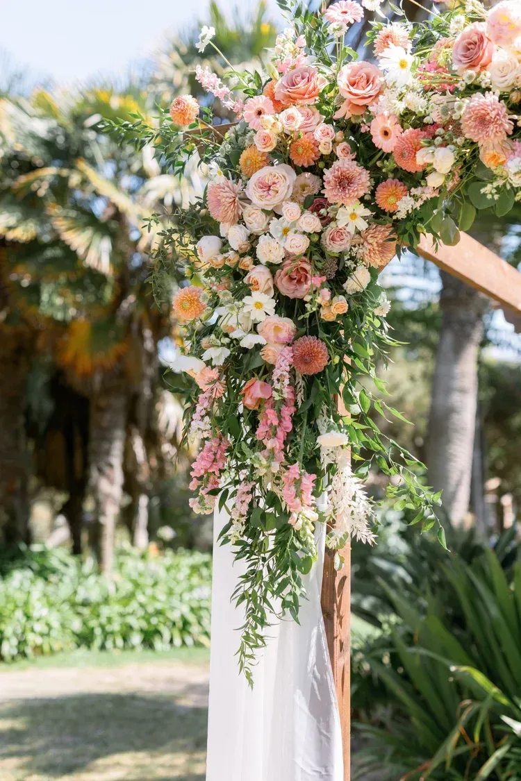 Floral wedding arch with pink and white roses and greenery in a sunlit garden