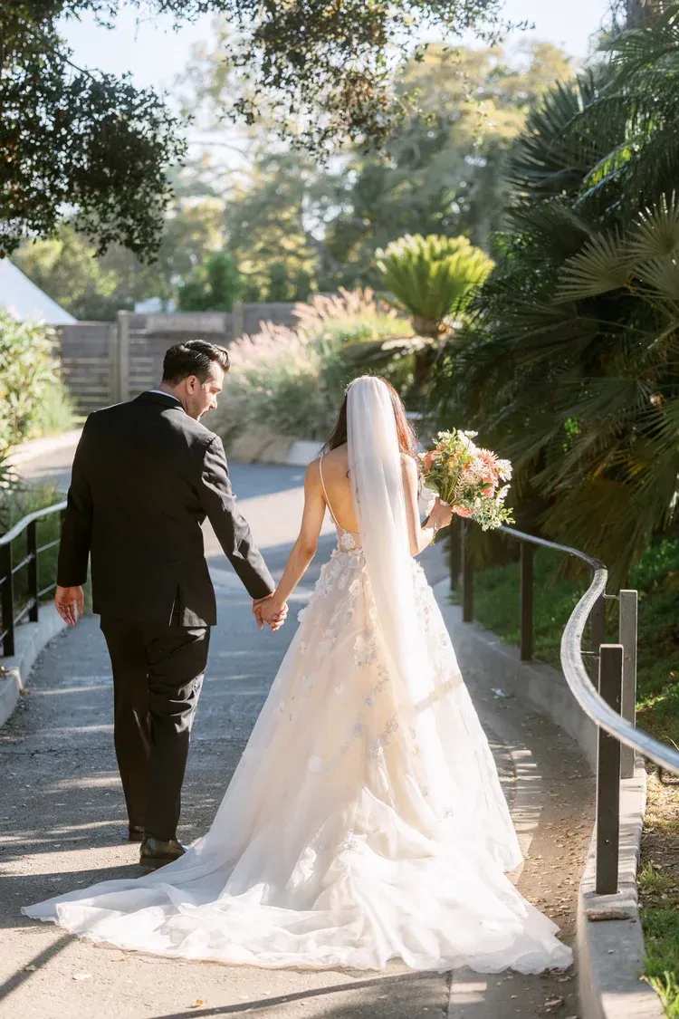 Bride and groom walking hand in hand down a garden path at an outdoor wedding