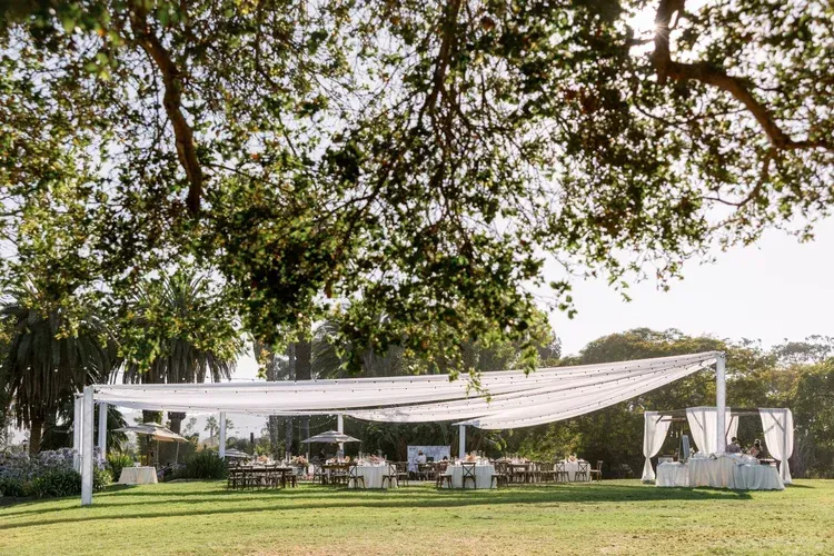 Outdoor wedding reception under white draped canopy on a grassy lawn beneath trees