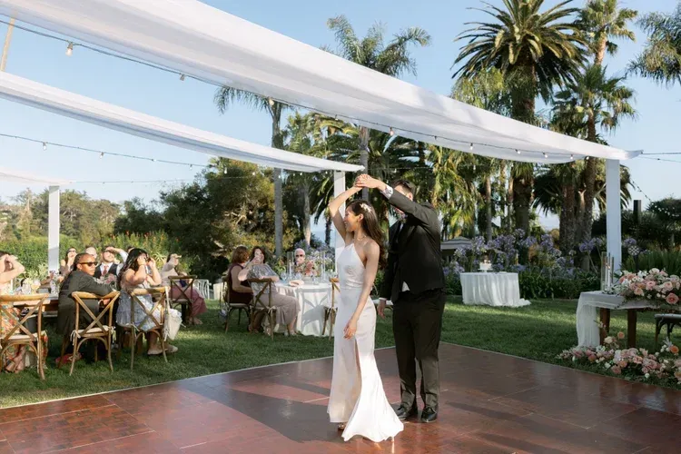 Couple dancing under a white canopy at an outdoor wedding reception with guests seated nearby