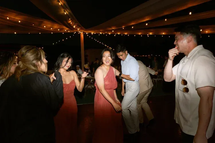 People dancing at a dimly lit party under string lights, with drinks in hand.