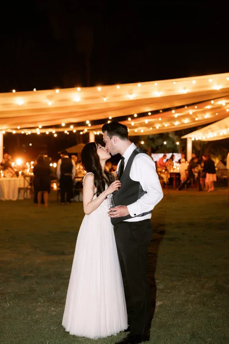 Couple dancing at an outdoor evening reception under string lights