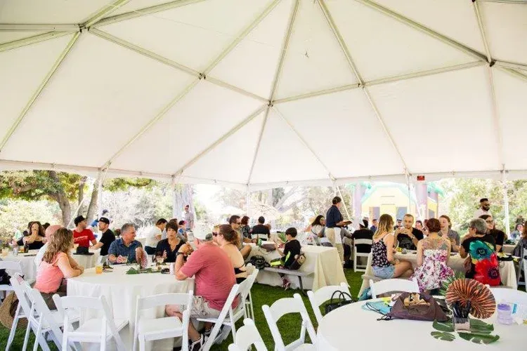 Guests seated at tables under a white event tent for a catered outdoor gathering