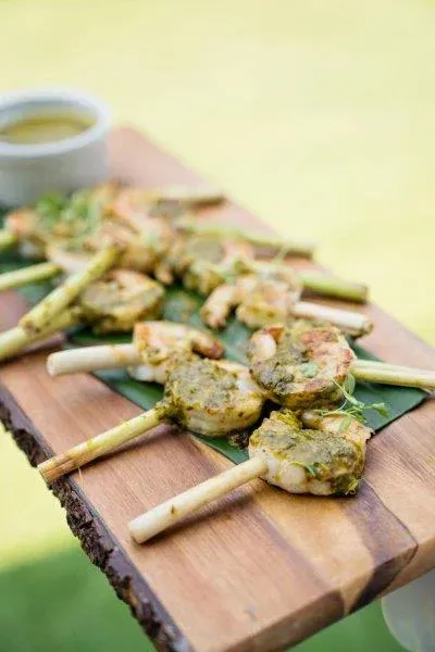 Grilled skewered appetizers on a wooden board with a dipping sauce in the background