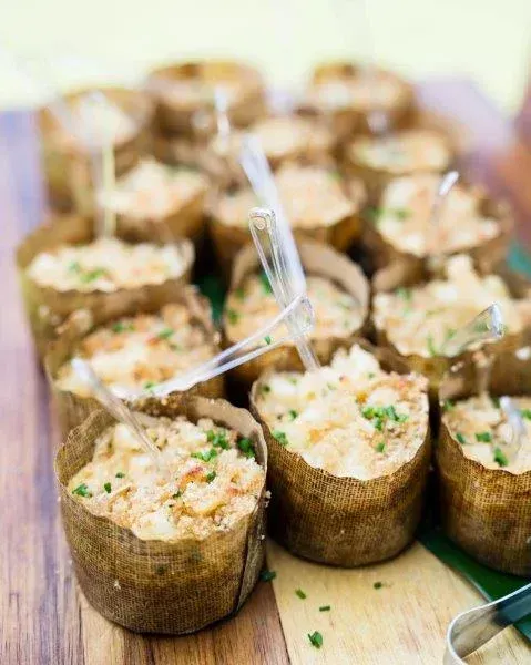Small cups of creamy appetizer salad in dark lettuce wraps, arranged on a wooden tray with plastic picks.