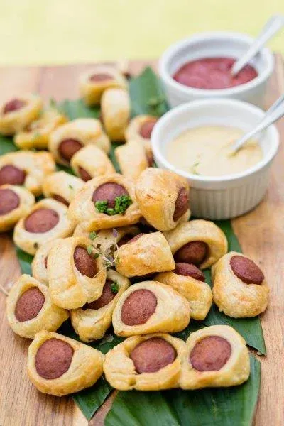 Golden sausage rolls on a wooden board with two dipping sauces