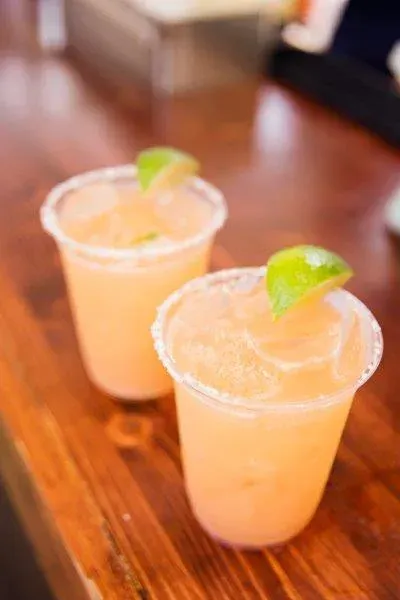 Two orange cocktails with lime wedges on a wooden table