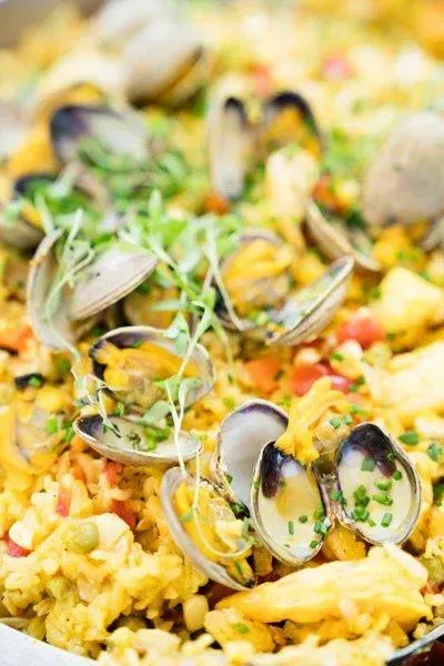 Seafood paella with mussels, shrimp, and yellow rice topped with peas and lemon wedges