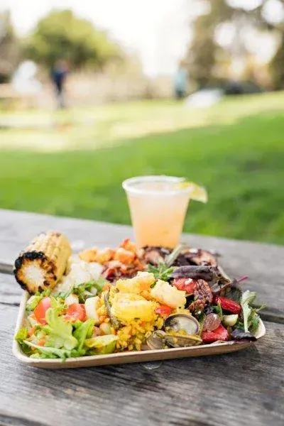 Salad bowl and drink on a table in a sunny park with blurred greenery behind
