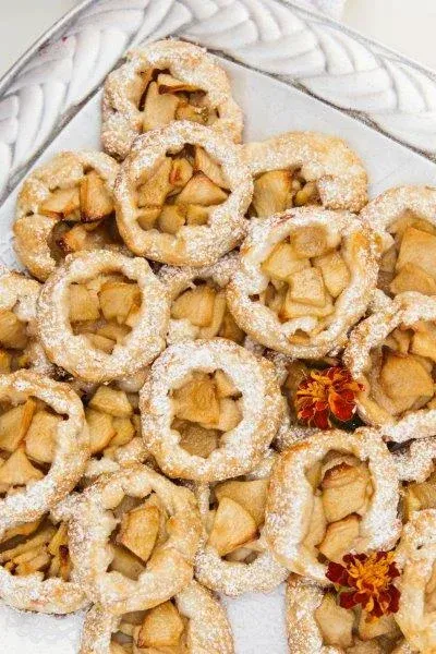 Powdered sugar pastries arranged on a plate, with some filled with jam or fruit