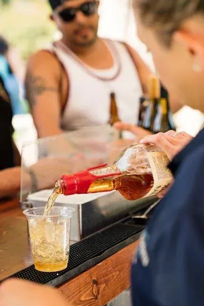 Bartender pouring amber drink into a glass at an outdoor bar