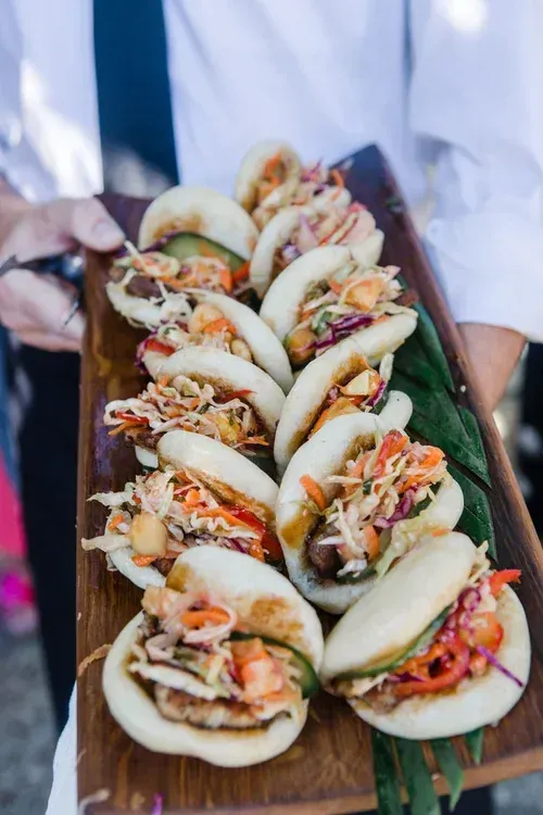 Tray of assorted bao buns with colorful fillings, held by a person in a white shirt