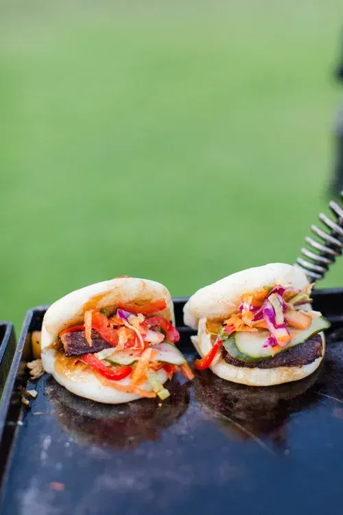 Two mini sandwiches with colorful vegetables on a grill, against a blurred green background