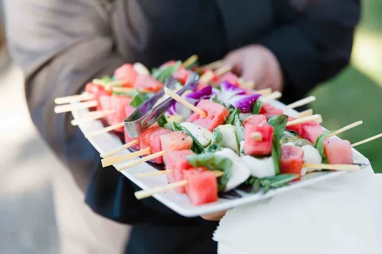 Tray of colorful fruit skewers being served outdoors by a person holding a plate