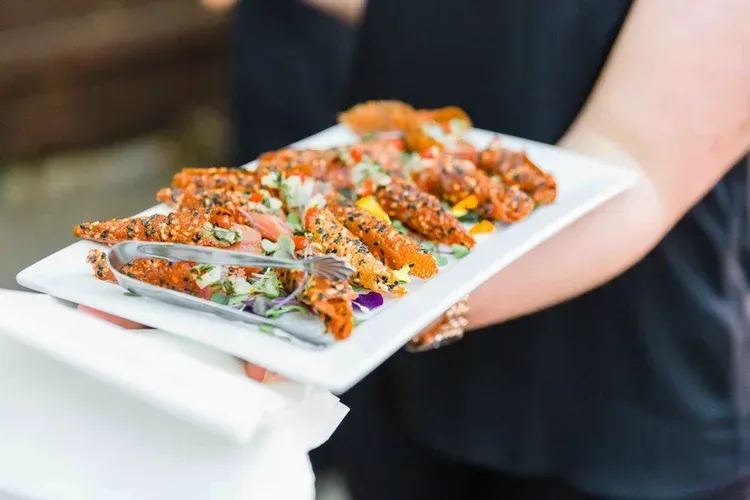 Platter of sliced, sauced appetizers garnished with herbs, being held on a tray by a person