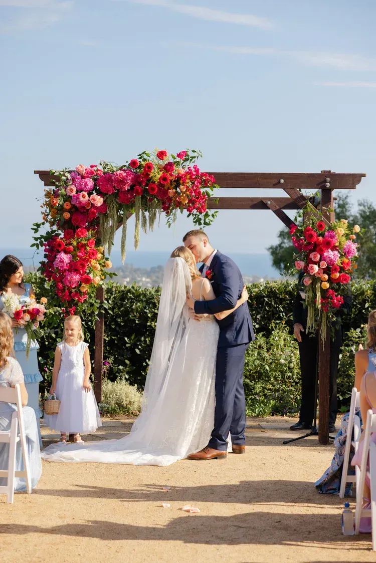 Bride and groom kissing beneath a flower-covered wedding arch outdoors