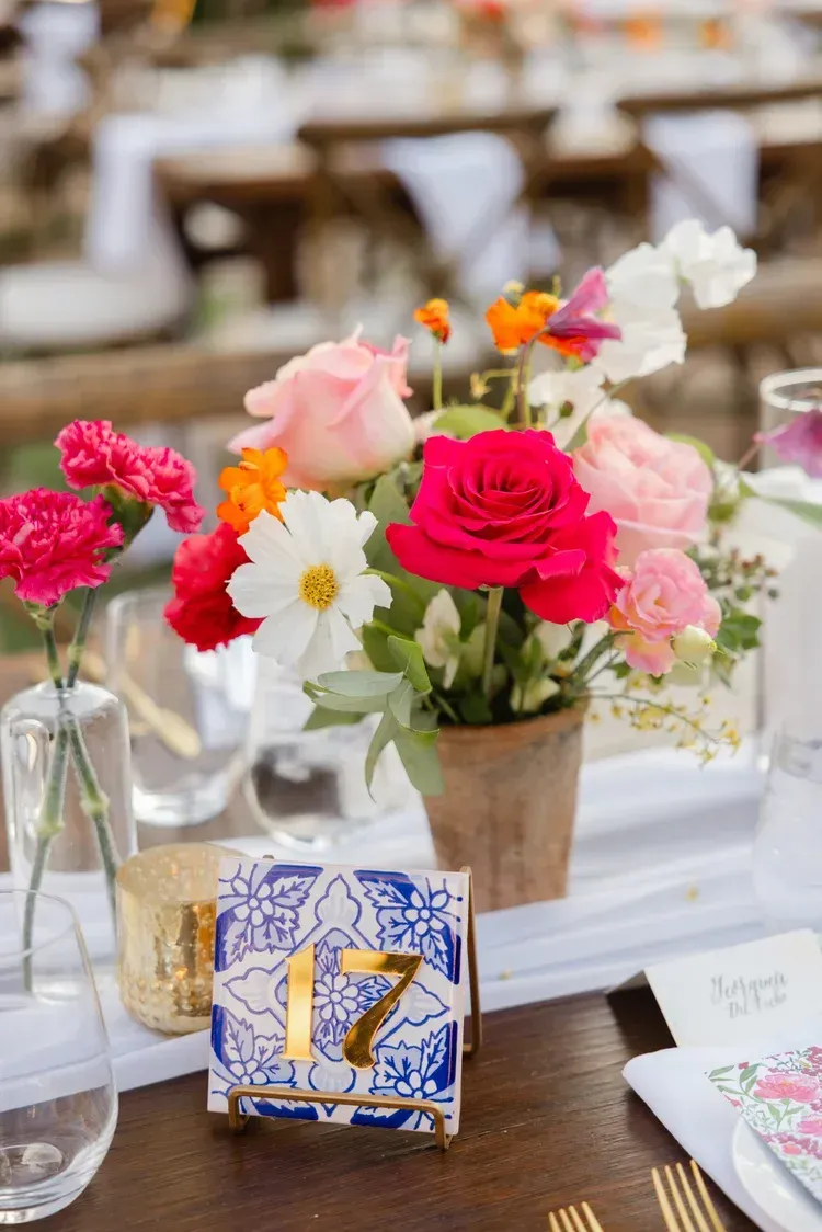 Bright floral table centerpiece with pink, red, and white flowers, plus a blue-and-gold table number 17.