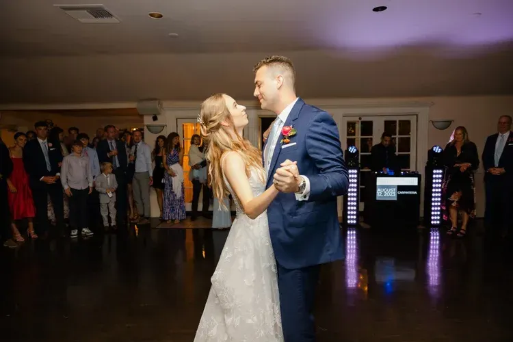 Bride and groom dance in a dimly lit reception hall with guests watching nearby