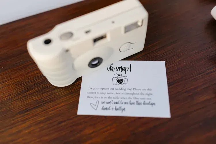 White instant camera on wooden table next to a small handwritten thank-you card