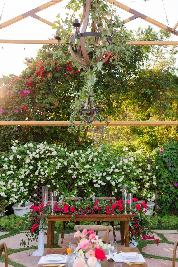 Flower-filled greenhouse with a bench, white blossoms, and pink hanging blooms under a wooden frame