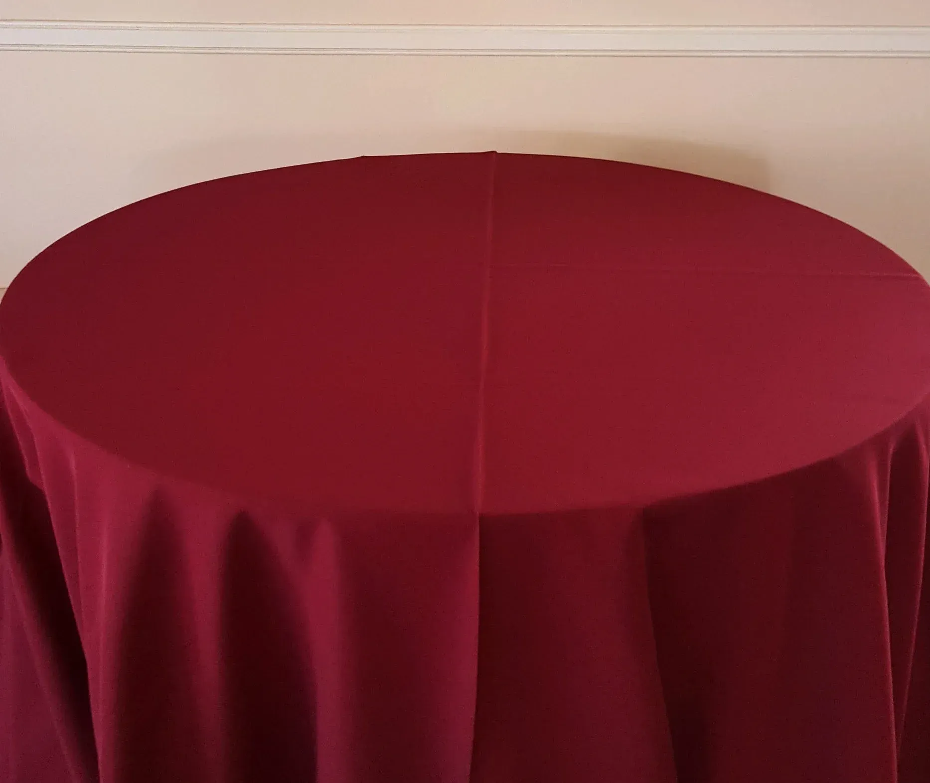 Round table covered with a deep red cloth against a beige wall.