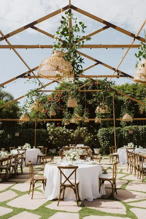Outdoor wedding reception under a tent with round tables, white linens, and hanging greenery decor