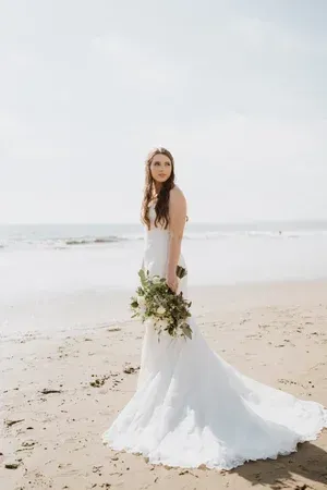 Bride in a white wedding dress holding a bouquet on a beach