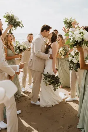 Couple kissing at a beach wedding ceremony with floral arrangements and seated guests